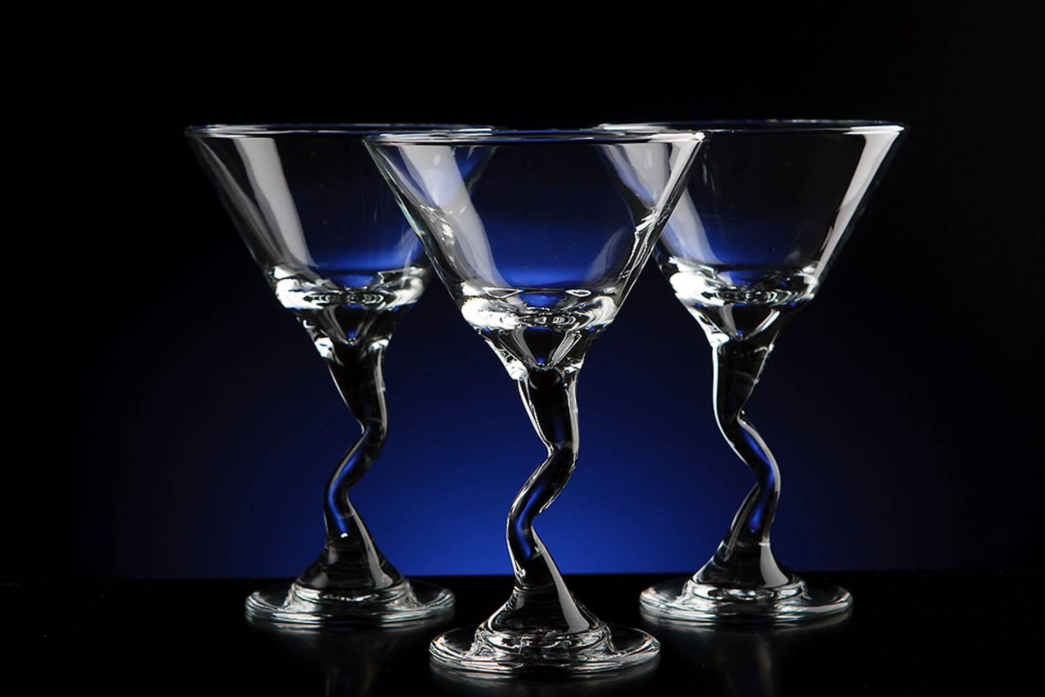 three martini glasses with crooked stems in front of a blue and black background
