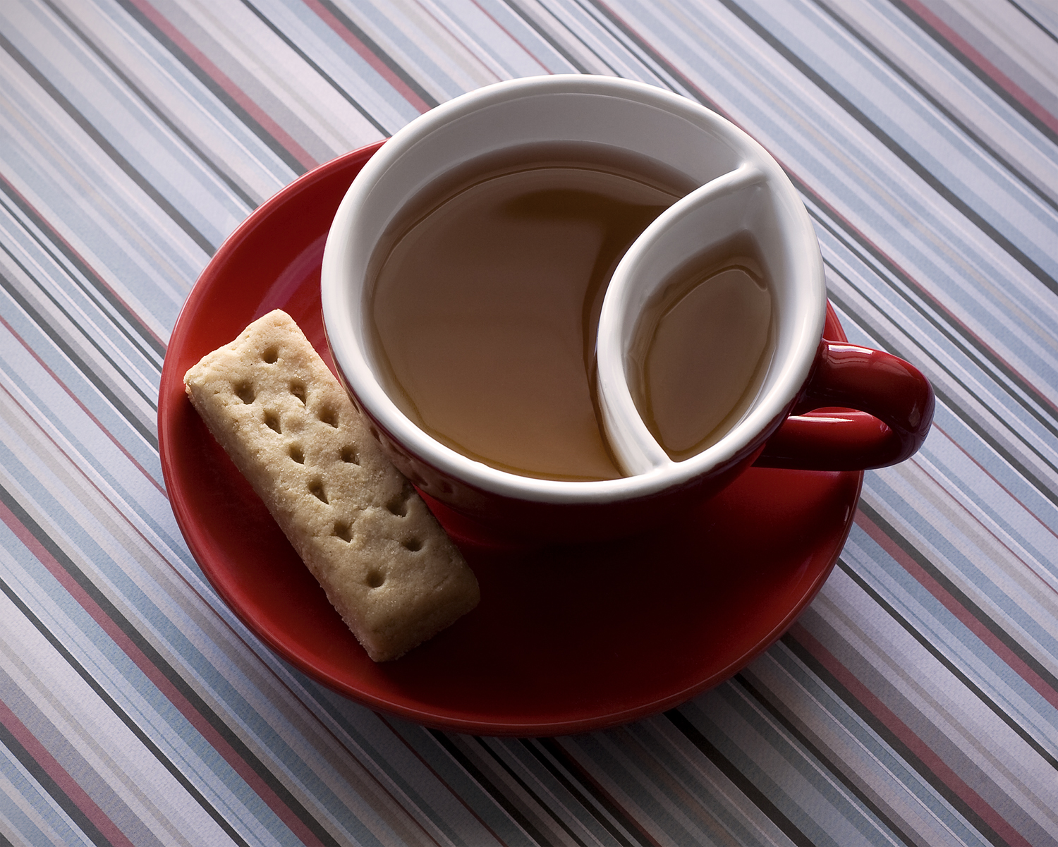 two section cup with tea and a biscuit on a red plate