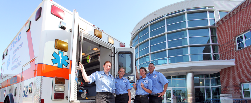 four students standing behind an ambulance with the doors open