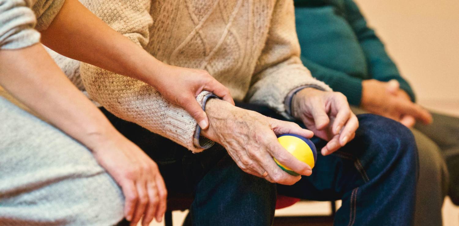elderly person holding a ball with person sitting next to them