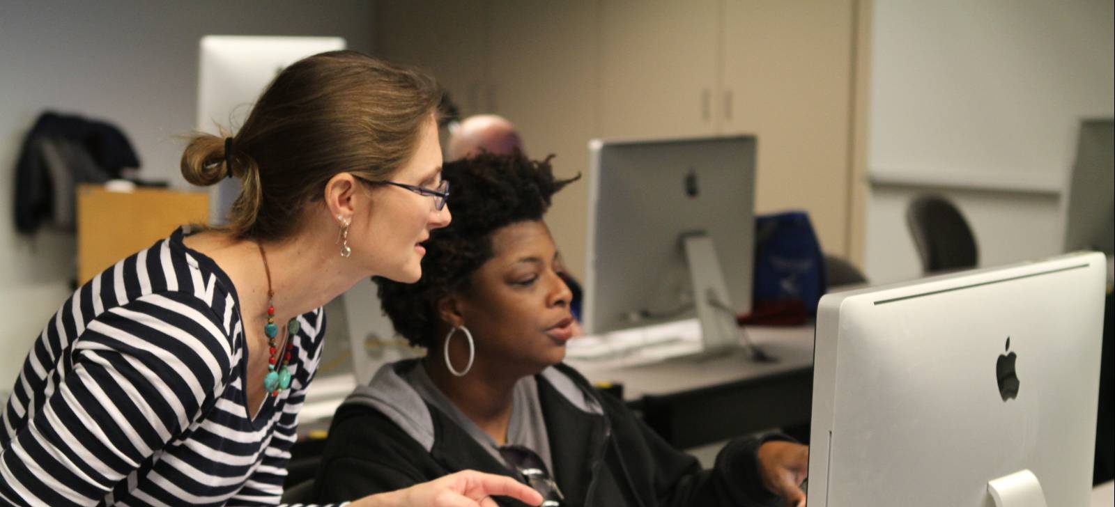 student a computer in black hoodie with women in striped shirt