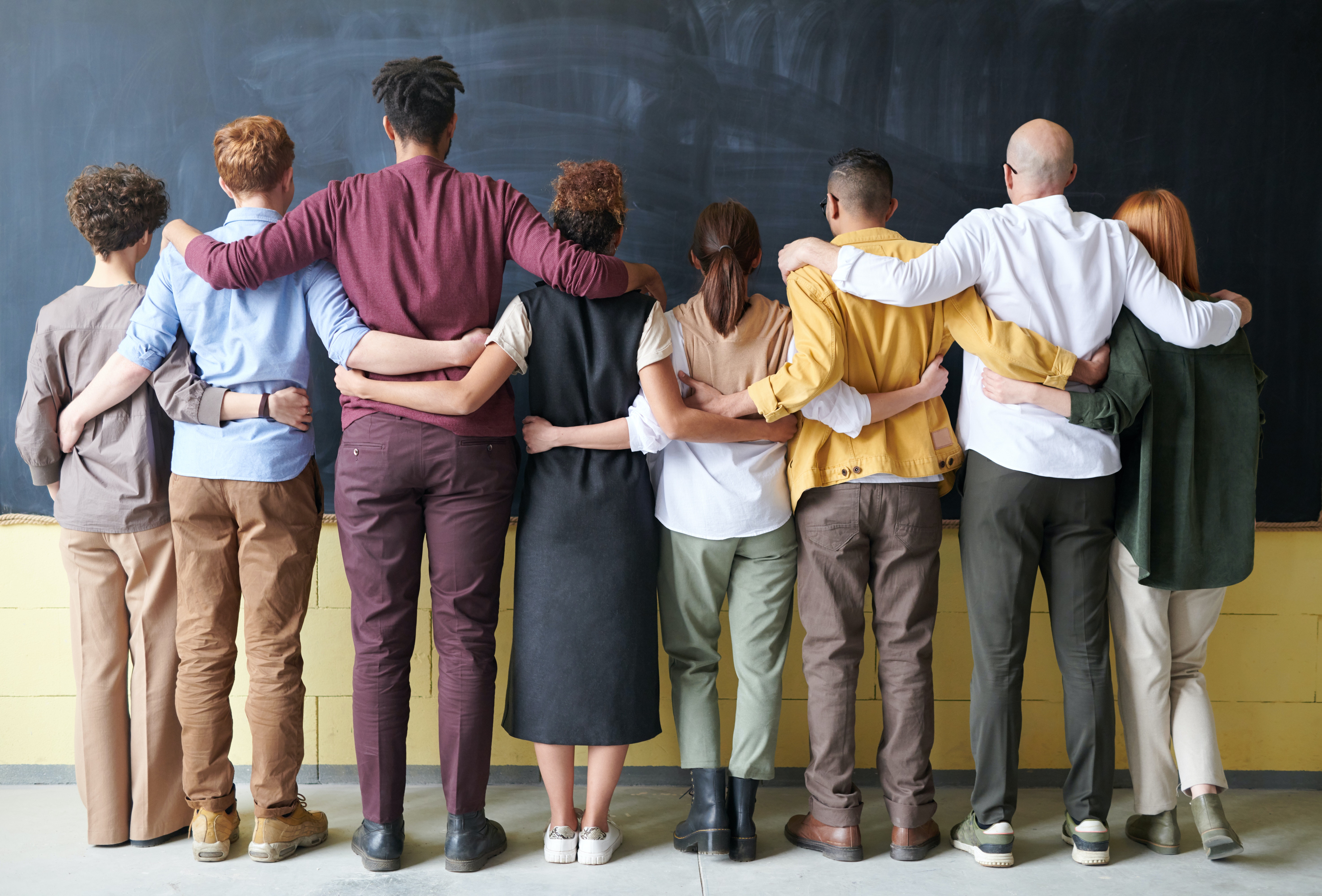 8 students in front of blackboard with their arms around each others shoulders or waist