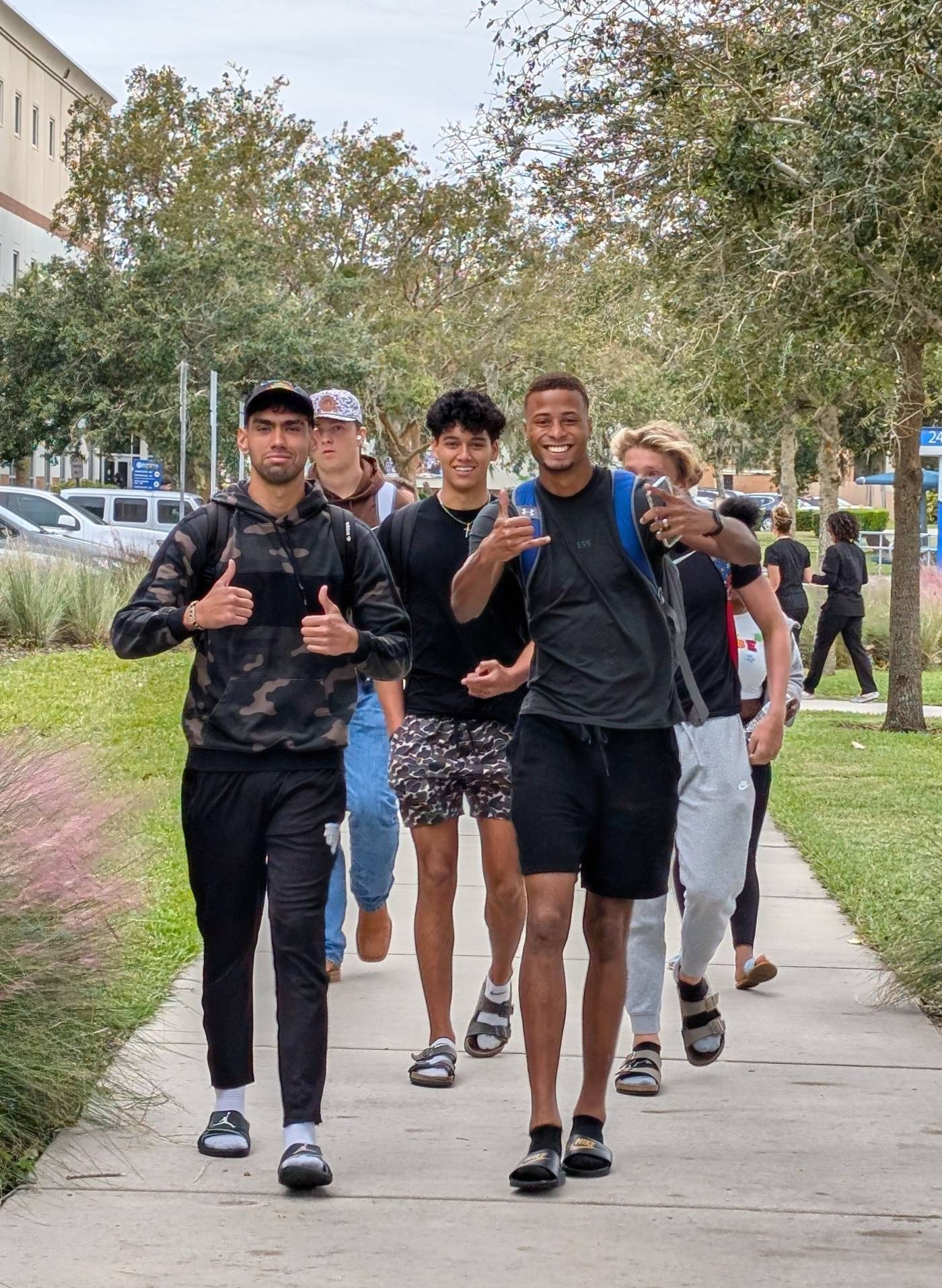 A grouip of male student walking toward the camera with thumbs up and smiling